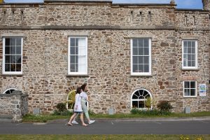 Two women walk past the large exterior of a pale brick Victorian building - the Castle Bude.