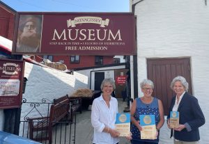 Three women standing outside Mevagissey Museum holding trophies
